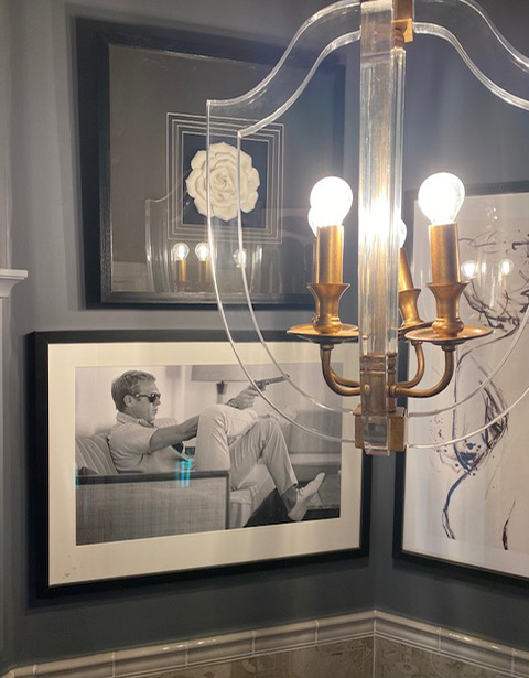 A stylish chandelier illuminates a black-and-white photograph of a man lounging on a couch, surrounded by modern wall art and a flower motif, contributing to a contemporary home decor aesthetic.