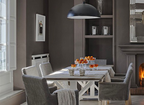 modern dining room featuring a wooden table set with fruit and drinks, surrounded by gray upholstered chairs, and a stylish pendant light overhead