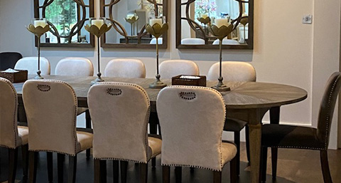 dining room with a round wooden table surrounded by elegant upholstered chairs and decorative candle holders, featuring mirrors in the background.