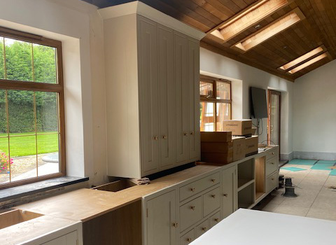 A partially furnished kitchen with light-colored cabinetry and boxes stacked on the counter, featuring large windows that let in natural light and a view of the green outdoors.